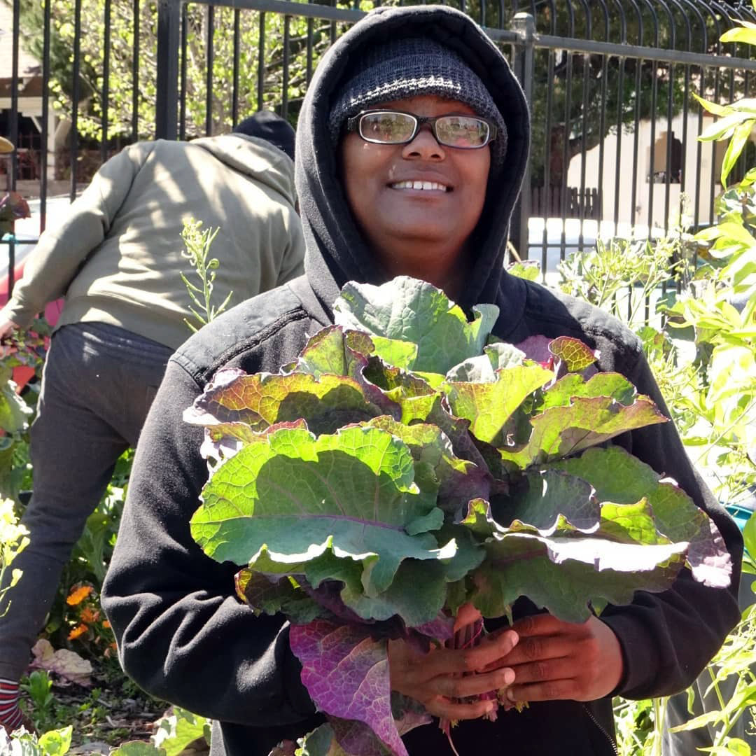 Photo of Karla from our permaculture workshop. She is smiling and holding a bunch of kale.